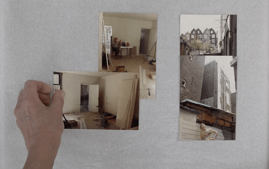 A hand arranges photographs of a house under construction on a large white sheet of paper