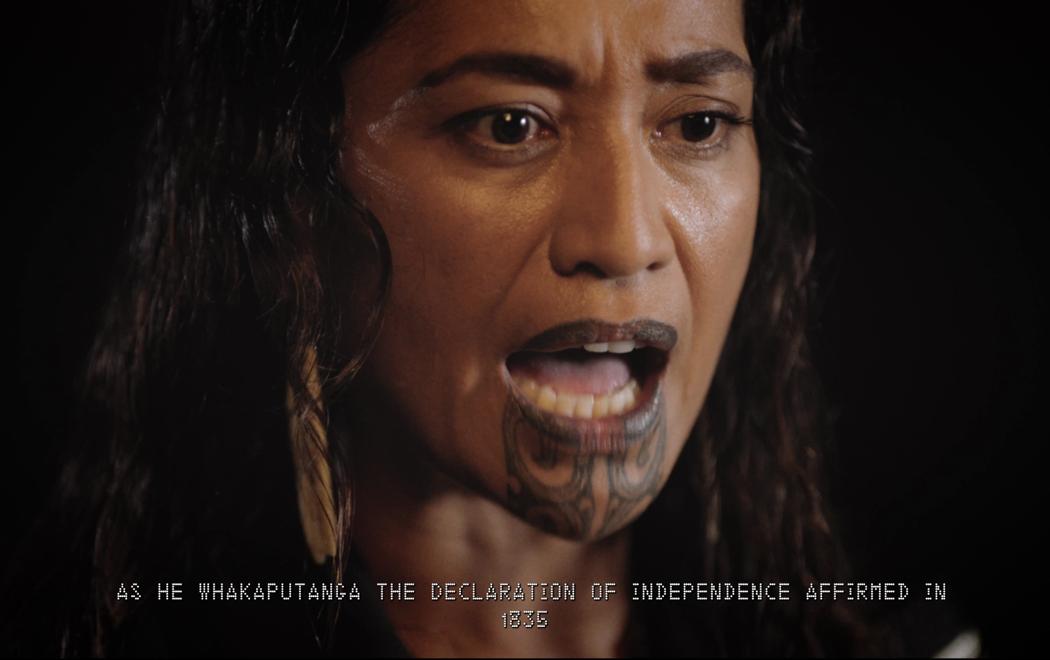 A close up of a woman with her mouth open as if speaking. Her gaze is fixed and serious. The text on the bottom of the screen says "As He Whakaputanga the Declaration of Independence Affirmed in 1835".