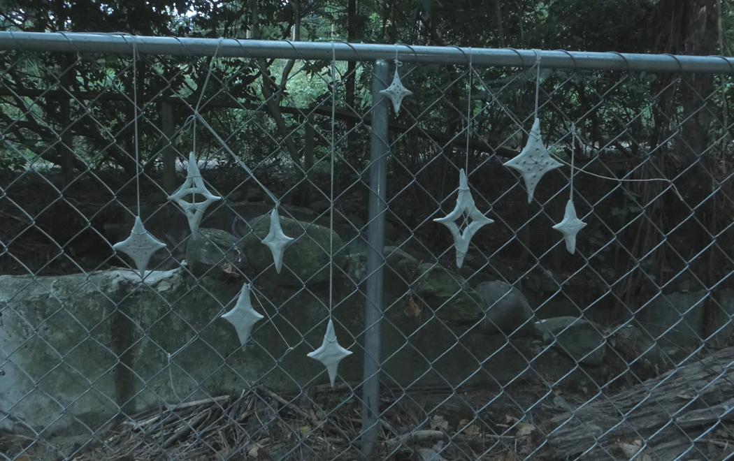 A cluster of nine handmade stars (representing Matariki) hang from a chain link fence.