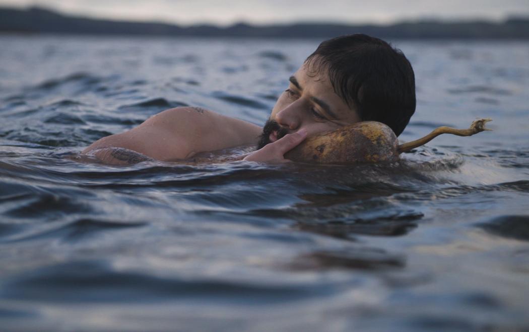 A man swims in a lake holding a gourd underneath his head.