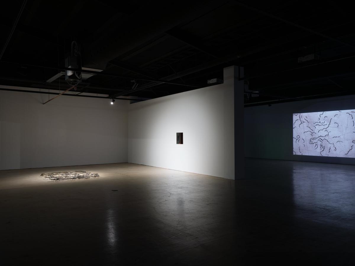In a gallery we see three artowrks, from left, on the floor a loose assembly of metal resembling a cloud, in the centre a hole in the wall approximately the size of a dumb waiter, and at right, a video projection of an animated cloud.