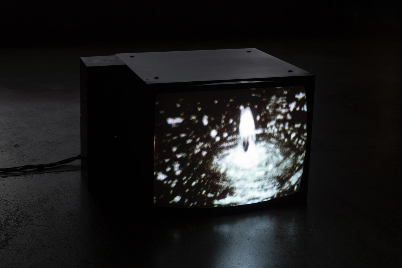 On a 4:3 cube video monitor we see a blurry black and white image of a fountain gushing upwards.